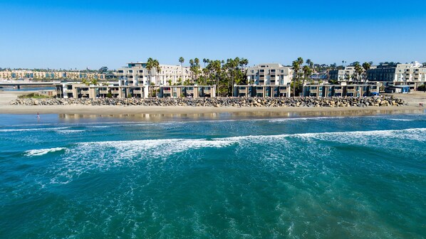 A beachfront hotel with multiple-story buildings, a rocky shoreline, and palm trees.