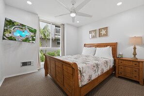 A bedroom with a wooden bed, a nightstand, a lamp, a ceiling fan, and a window with a view of greenery. - Absolute Beach Front Cottage! Panoramic Views E20 North Coast Village (Oceanside)