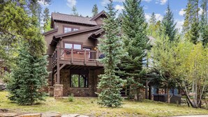 A two-story log cabin with a stone foundation, a balcony, and a stone retaining wall in front.
