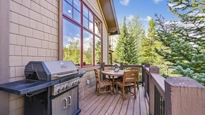 An outdoor deck with a built-in grill, wooden chairs, and a table.