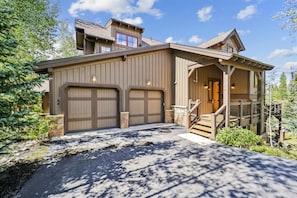 Stunning two-story residence with a central entrance and garage doors, set amidst lush greenery.