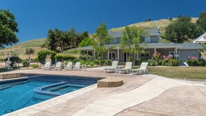A residential property with a swimming pool, outdoor seating, and a hillside backdrop.