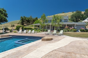 A residential property with a swimming pool, outdoor seating, and a hillside backdrop.