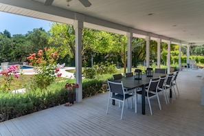An outdoor patio with a table and chairs, surrounded by lush greenery and a swimming pool.