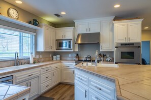 A modern kitchen with white cabinetry, a stainless steel range hood, and a built-in oven.
