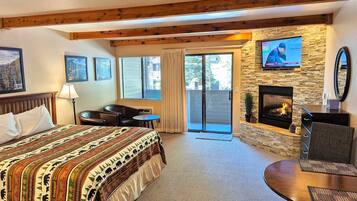 A hotel room with a bed, a fireplace, a television, a desk, and a balcony with a sliding door.