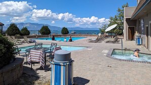 A pool area with lounge chairs, a hot tub, and a view of the sea and mountains.