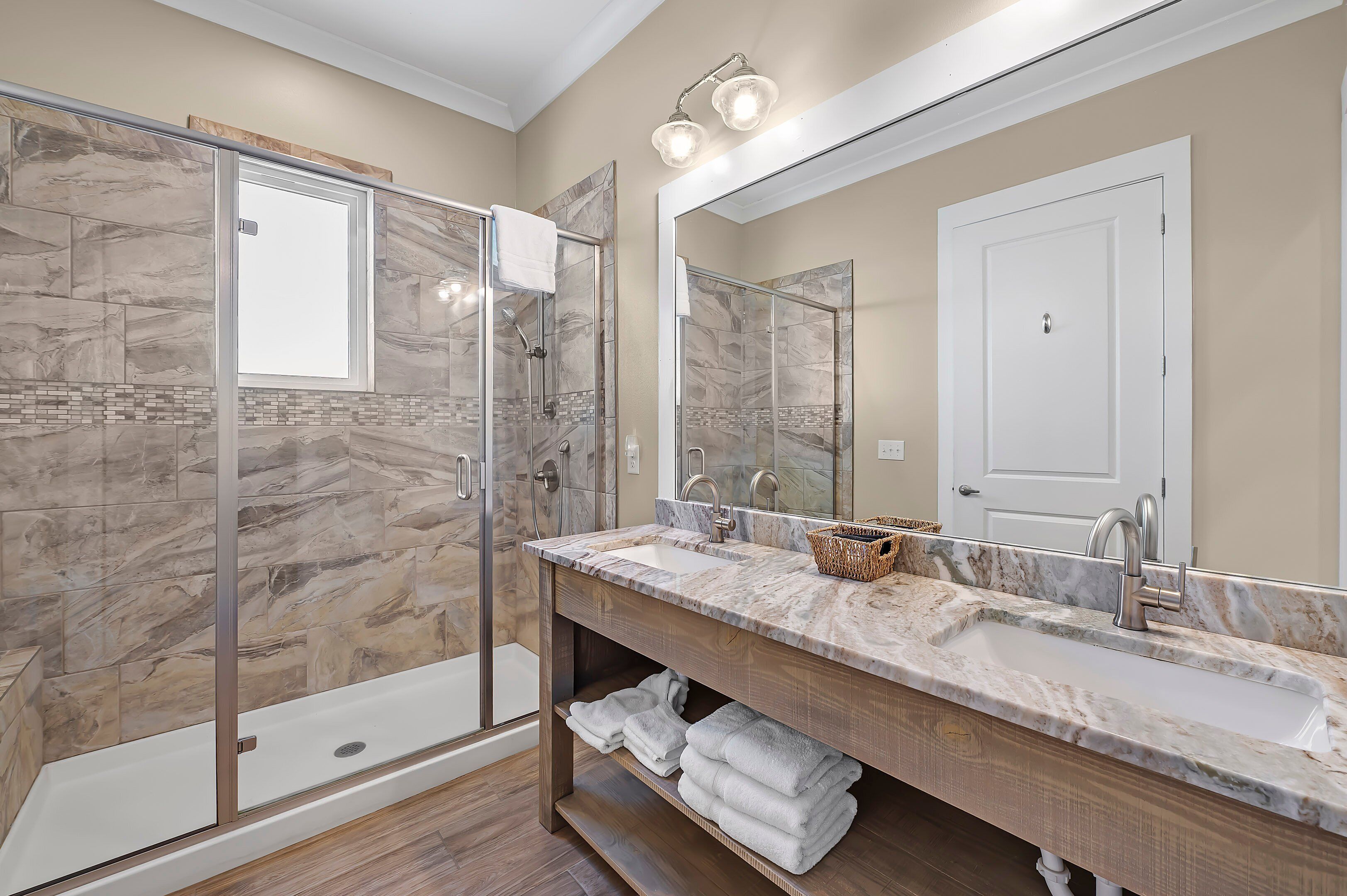 A modern bathroom with a glass-enclosed shower, a large mirror, and a marble countertop.