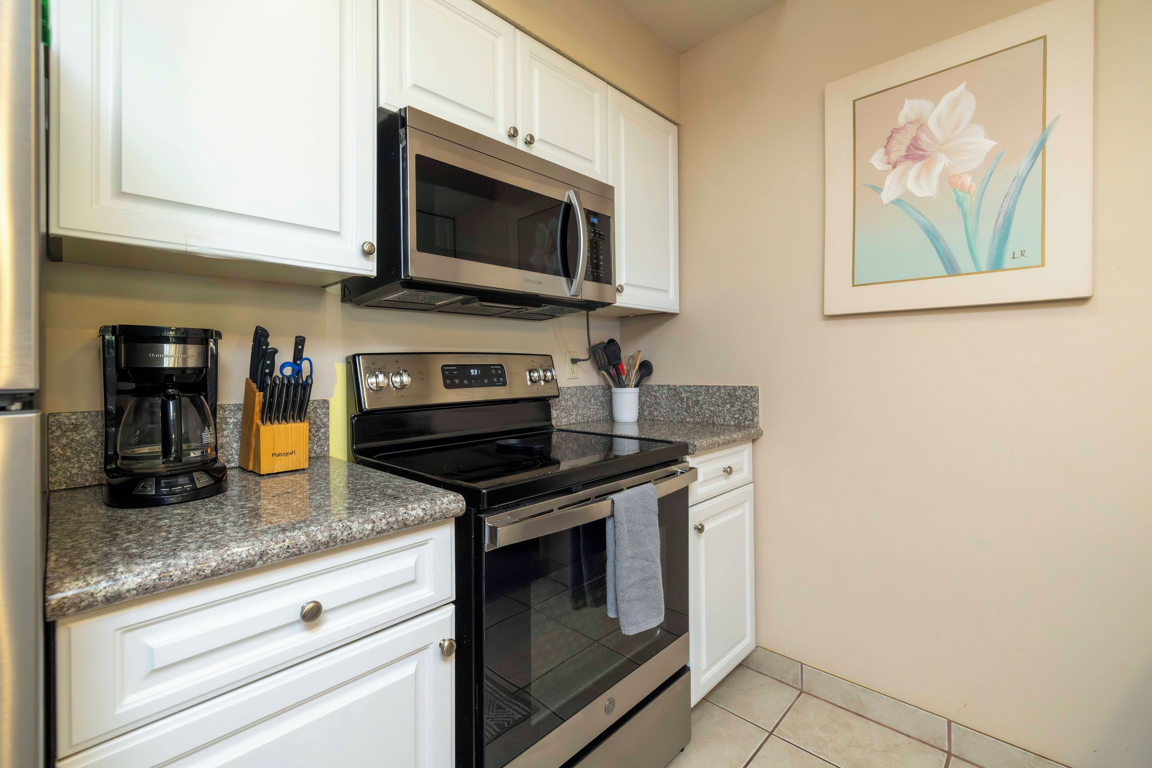 A kitchen with white cabinets, a microwave, a coffee maker, and a stove.