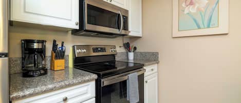 A kitchen with white cabinets, a microwave, a coffee maker, and a stove.