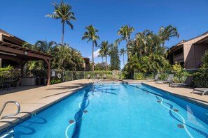 A swimming pool with a clear blue water design, surrounded by palm trees and lounge chairs.