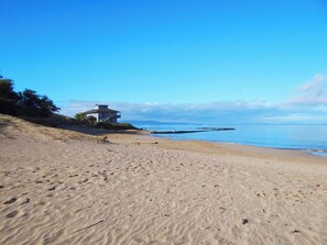 A beach with a house on a hill, a clear sky, and calm sea.