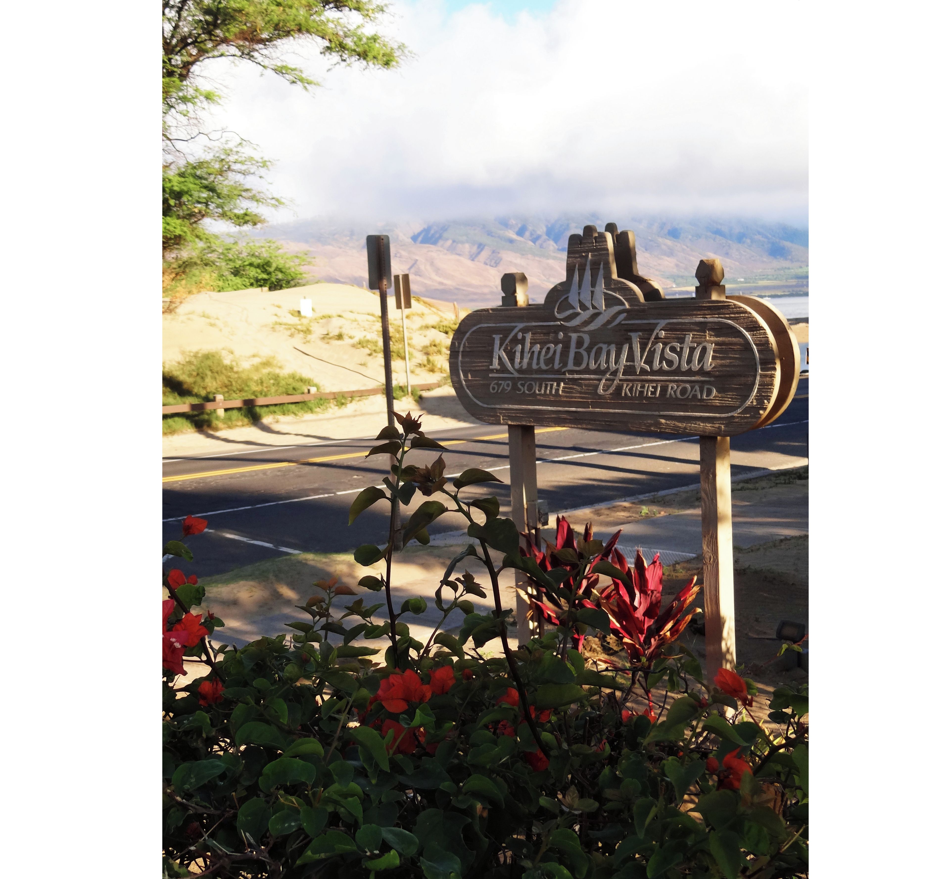 Un panneau indiquant « Kihei Bay Vista », avec une vue sur les montagnes et une route.