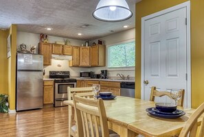 A kitchen with wooden cabinets, a refrigerator, stove, microwave, and a dining table with chairs.
