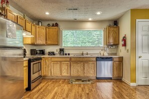 A kitchen with wooden cabinets, stainless steel appliances, a window with blinds, and a door.