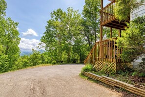 A gravel driveway leading to a wooden staircase with a lattice railing, surrounded by lush greenery and trees.