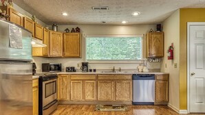 Una cocina con armarios de madera, electrodomésticos de acero inoxidable, una ventana con persianas y un extintor.