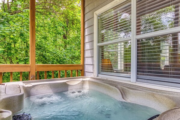 A hot tub on a wooden deck with a view of lush greenery.