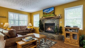 Una sala de estar con chimenea, un sofá, una mesa de centro y un televisor instalado en la pared.