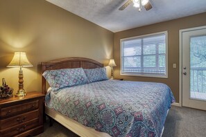 A bedroom with a bed, two bedside lamps, a wooden nightstand, a dresser, a ceiling fan, and a window with blinds.