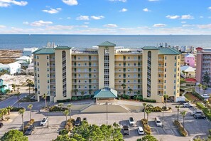 A multi-story hotel with a central courtyard, parking area, and a view of the ocean.