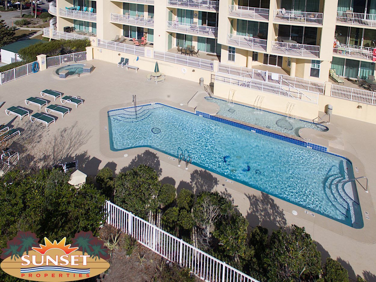A rooftop pool area with lounge chairs and a swimming pool, surrounded by a building with balconies.