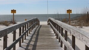 Ein hölzerner Steg führt zu einem Strand, entlang dessen beide Seiten 'KEEP OUT'-Schilder aufgestellt sind.