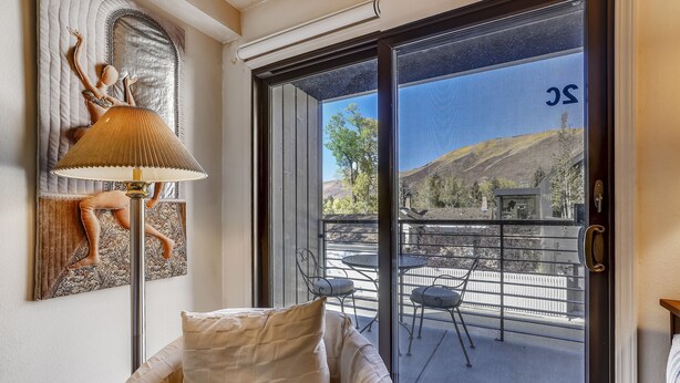 A room with a sofa, a lamp, and a sliding glass door leading to an outdoor patio with chairs and a table. - Charming condo in the core, dynamite location (Aspen)
