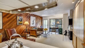 A modern living room with a wooden wall, a sofa, a coffee table, a kettle, and a television. - Charming condo in the core, dynamite location (Aspen)