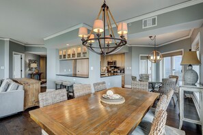 Un vaste espace de salle à manger avec une table en bois et des chaises en osier, une cuisine dotée de meubles en bois et un lustre orné de plusieurs luminaires.