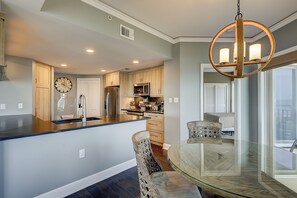 A modern kitchen with a central island, stainless steel appliances, and a dining area with a glass table and wicker chairs. - Beautiful 3 bed oceanfront villa located on the 4th floor in Palmetto Dunes! (Hilton Head Island)
