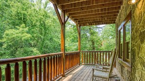 A wooden deck with a stone wall, a rocking chair, and a view of a forest.