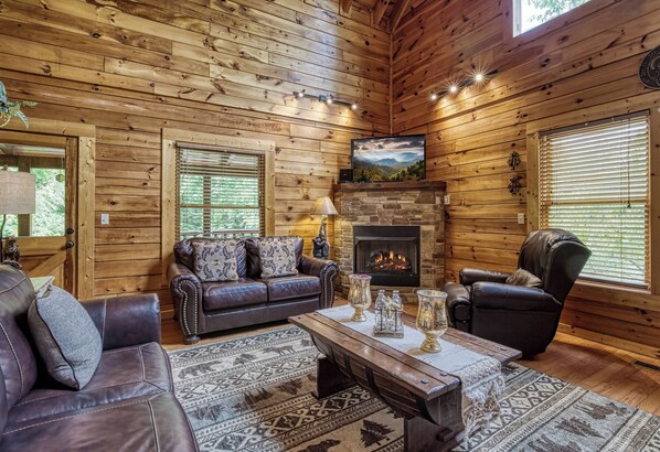A log cabin interior with a fireplace, leather furniture, and a large window.