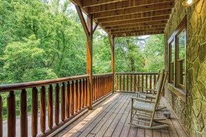 A wooden deck with a railing, a rocking chair, and a stone wall.