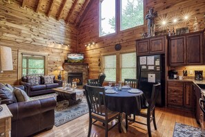 A log cabin interior with a living room, dining area, fireplace, and kitchen.