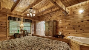 A wooden cabin interior with a large bed, a wooden cabinet, a table with chairs, and a bathtub.