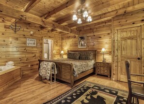 A wooden cabin bedroom with a bed, bedside lamps, a rug, and a wooden door.