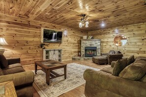 A cozy log cabin interior with a fireplace, a television mounted on the wall, and a comfortable seating area with a coffee table.