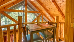 Ein Holzblock-Interieur mit einem Esstisch und Bänken, einem Deckenventilator und einem Fenster mit Blick auf Bäume.