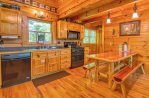 Interior de una cabaña de madera con cocina, que incluye armarios de madera, microondas, estufa y una mesa de comedor con bancos.