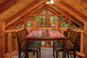 Una mesa de comedor de madera con sillas en una cabaña con techo inclinado y vistas a árboles.