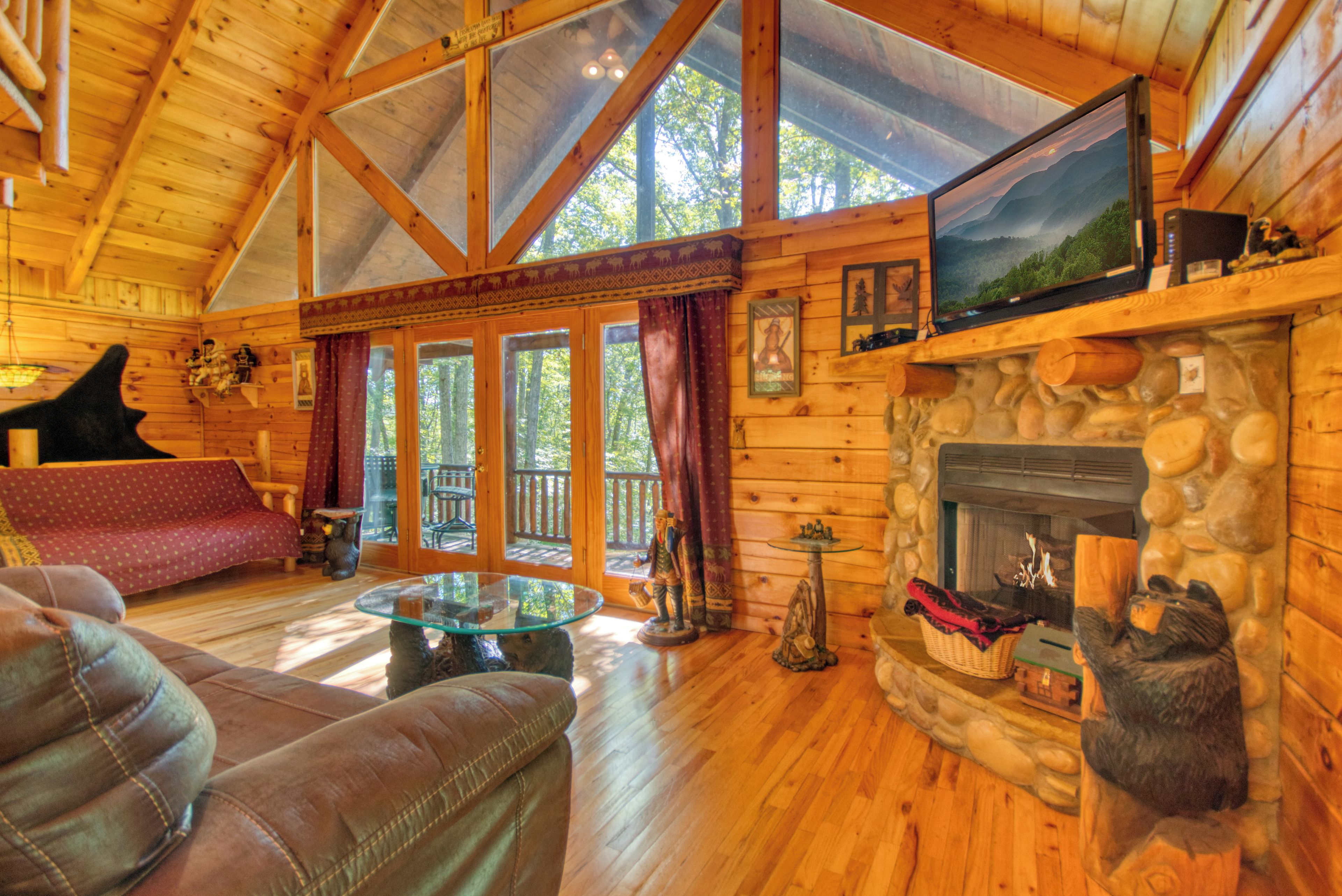 L’intérieur d’un chalet chaleureux, avec une cheminée en pierre, des murs en bois, une table basse en verre, un canapé rouge et un téléviseur fixé au mur.