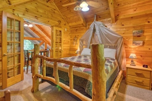 Un dormitorio de cabaña de madera con una cama, una mesita de noche, una lámpara, una ventana y una puerta.