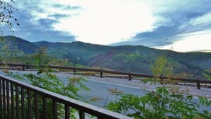 A scenic view from a balcony with a metal railing overlooking a road and hills. - Cozy Luxury Studio with Fireplace, Prime Location & Summer Adventure! (Deer Valley)