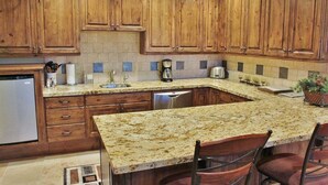 A kitchen with wooden cabinets, granite countertops, a built-in dishwasher, and a coffee maker. - Cozy Luxury Studio with Fireplace, Prime Location & Summer Adventure! (Deer Valley)