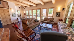 A spacious living room with a high ceiling, large windows, a sofa set, a coffee table, and a patterned rug. - Le Petit Soliel - In-Town Home, Ready for Your Whole Family! (Salida)