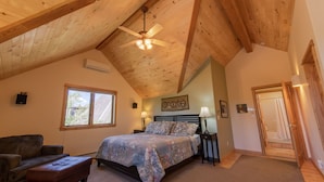 A bedroom with a wooden ceiling, a bed with a patterned bedspread, a nightstand with a lamp, a window, and a door leading to a bathroom. - Le Petit Soliel - In-Town Home, Ready for Your Whole Family! (Salida)