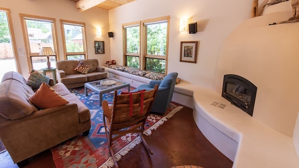 A cozy living room with a fireplace, large windows, and a mix of seating options including a sofa, chairs, and a bench. - Le Petit Soliel - In-Town Home, Ready for Your Whole Family! (Salida)