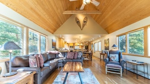A spacious living room with a wooden ceiling, large windows, a sectional sofa, a coffee table, and a fireplace. - Fox Haven at Summerwood Neighborhood, Community Pool+Clubhouse, Private Decks (Dillon)