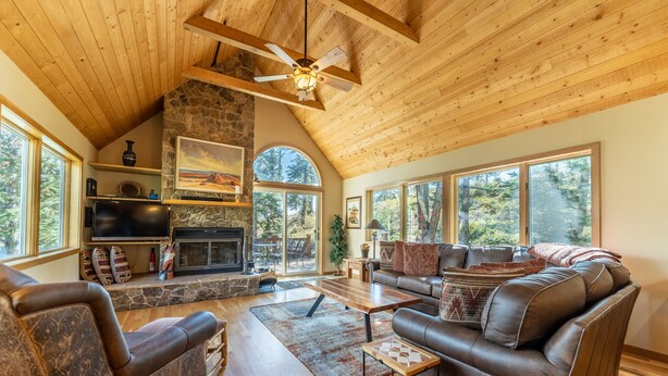 A spacious living room with a stone fireplace, leather sofas, and large windows offering a view of the outdoors. - Fox Haven at Summerwood Neighborhood, Community Pool+Clubhouse, Private Decks (Dillon)